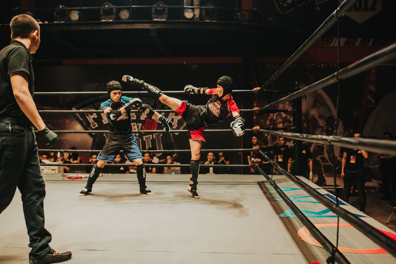 Intense kickboxing match with fighters in action inside a crowded indoor arena.